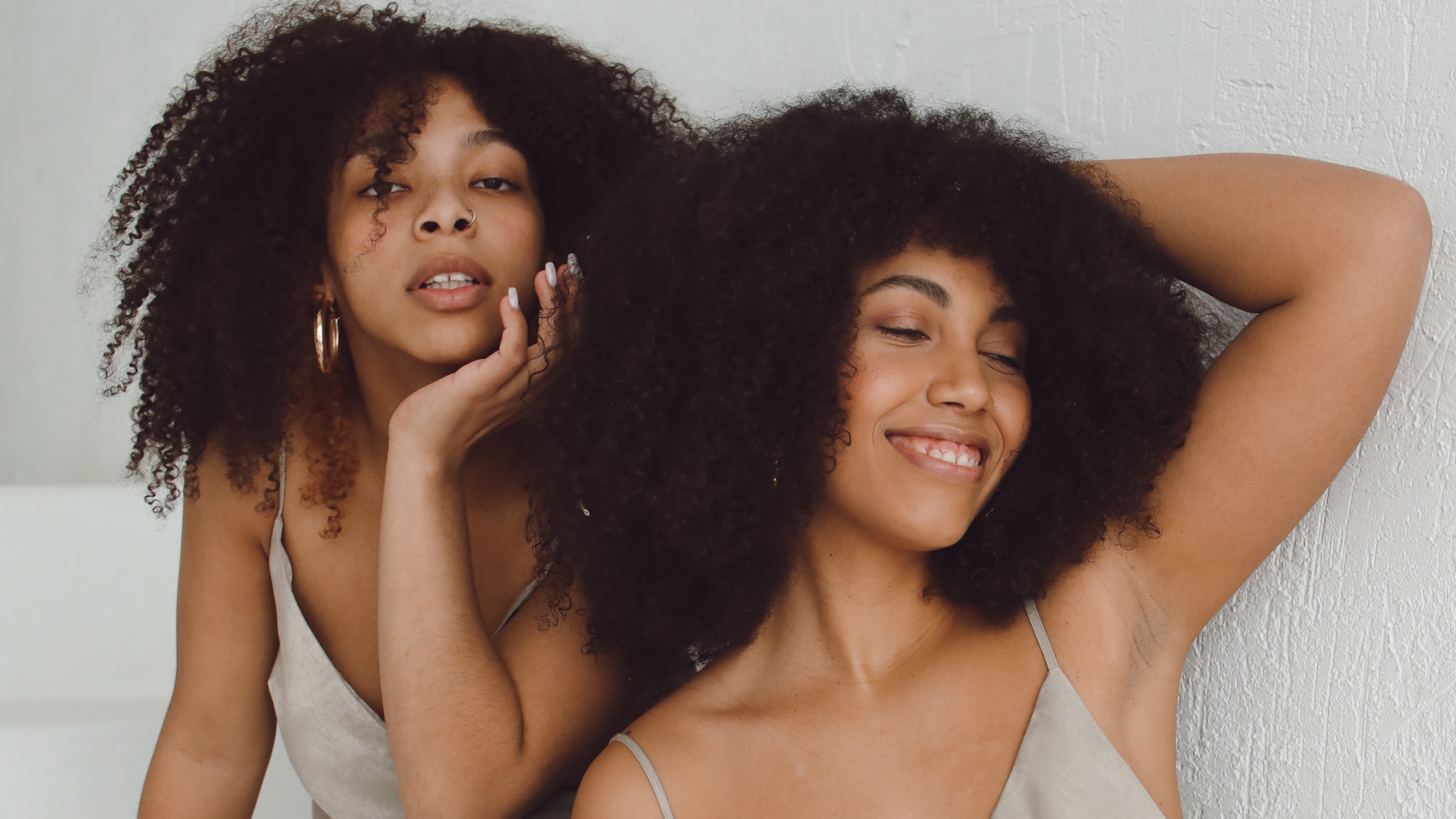 two women with curly hair posing against each other