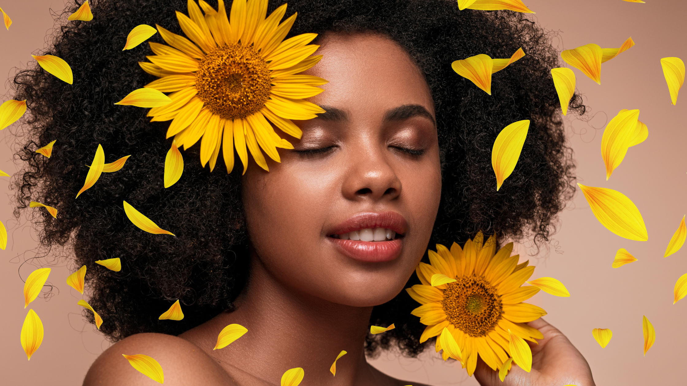 Woman with healthy natural curly hair surrounded by sunflower petals.